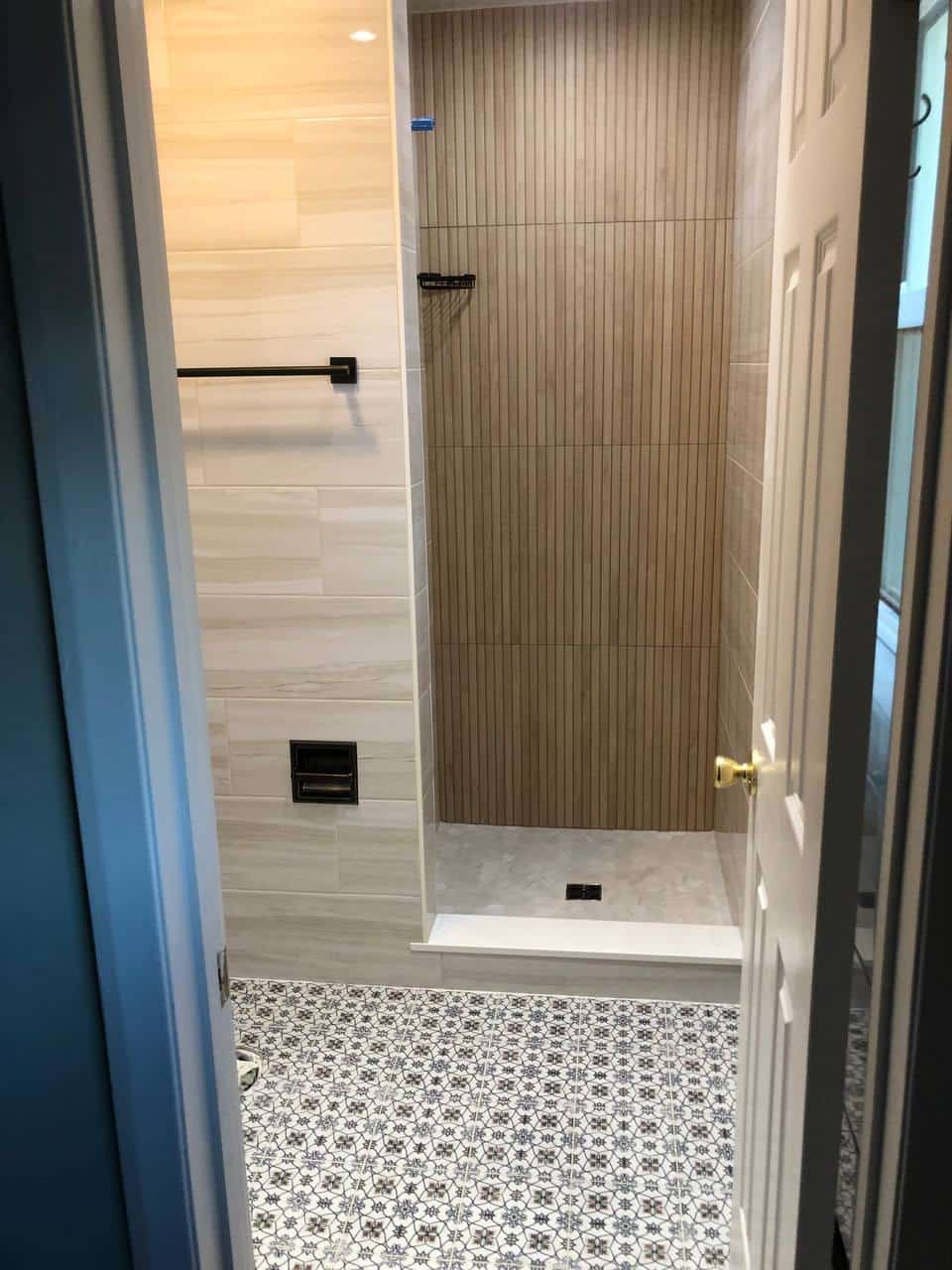 Finished walk-in shower with gray wall tile, mosaic floor, niche, and glass door