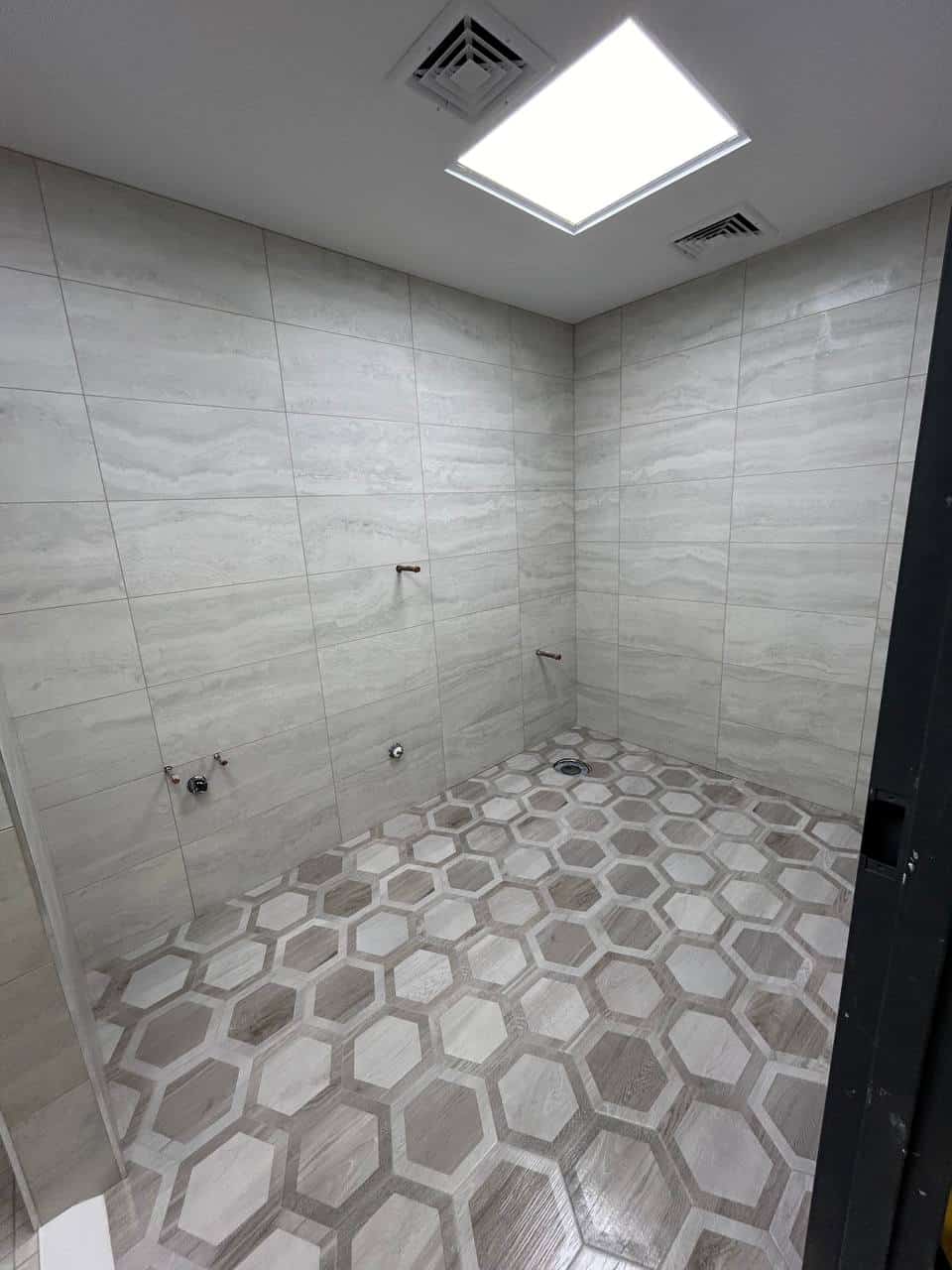 Walk-in shower with large gray wall tile, pebble floor, bench, niche, and skylight