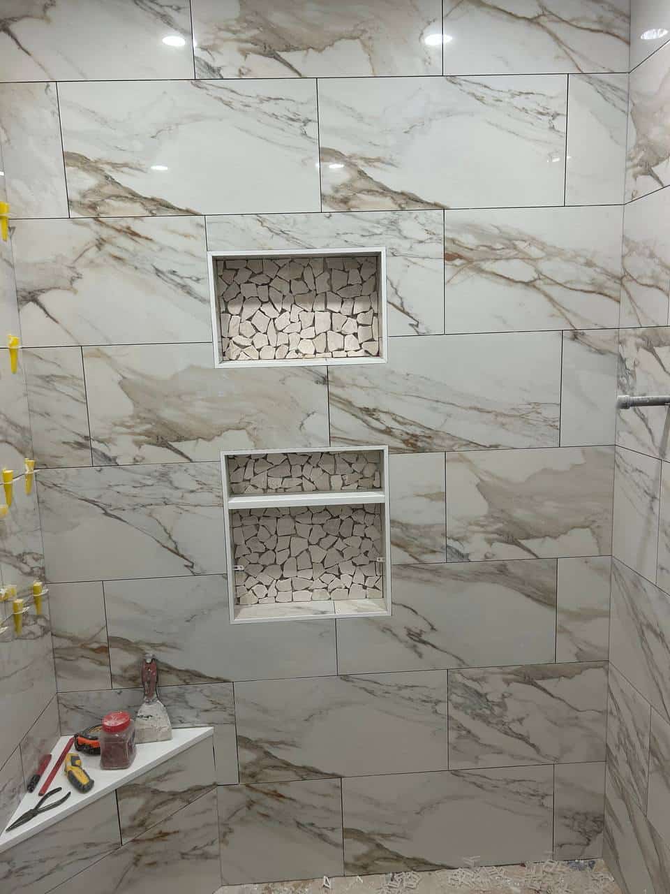 Marble-look shower wall tile with two recessed niches and mosaic niche backs