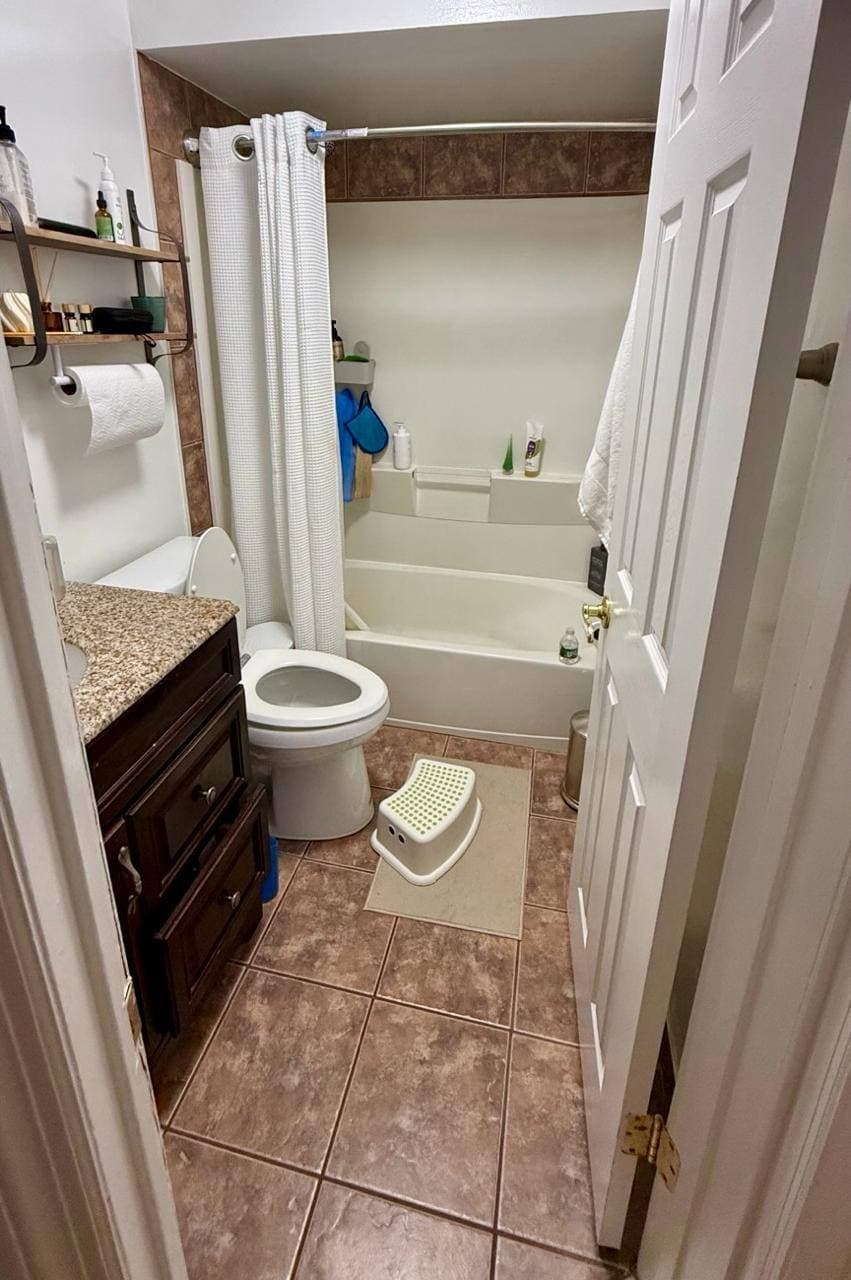 Compact bathroom with older vanity, floor tile, toilet, and tub before remodeling