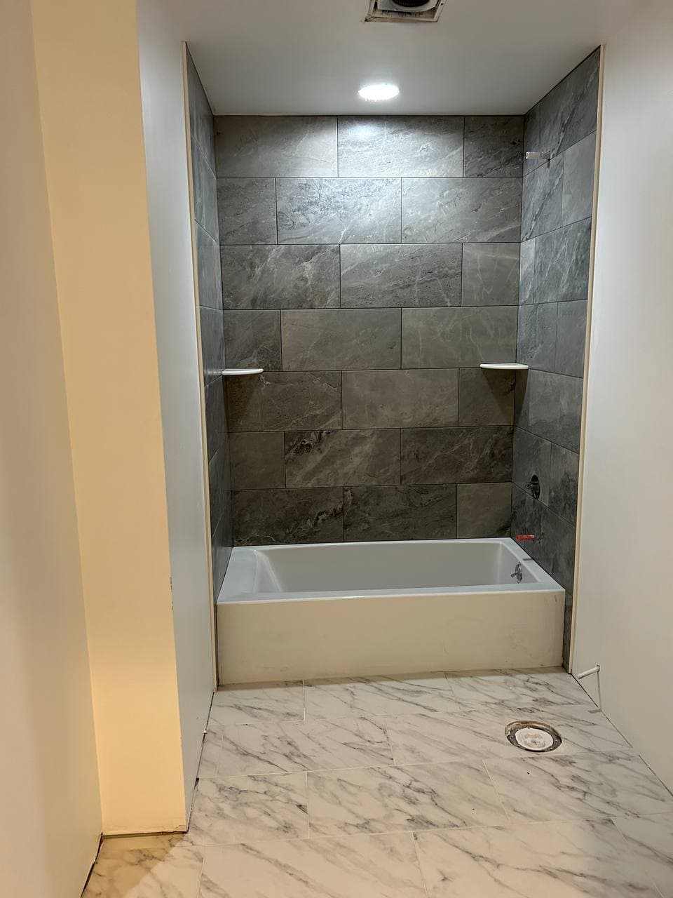 Remodeled bathtub alcove with dark gray wall tile and marble-look bathroom floor