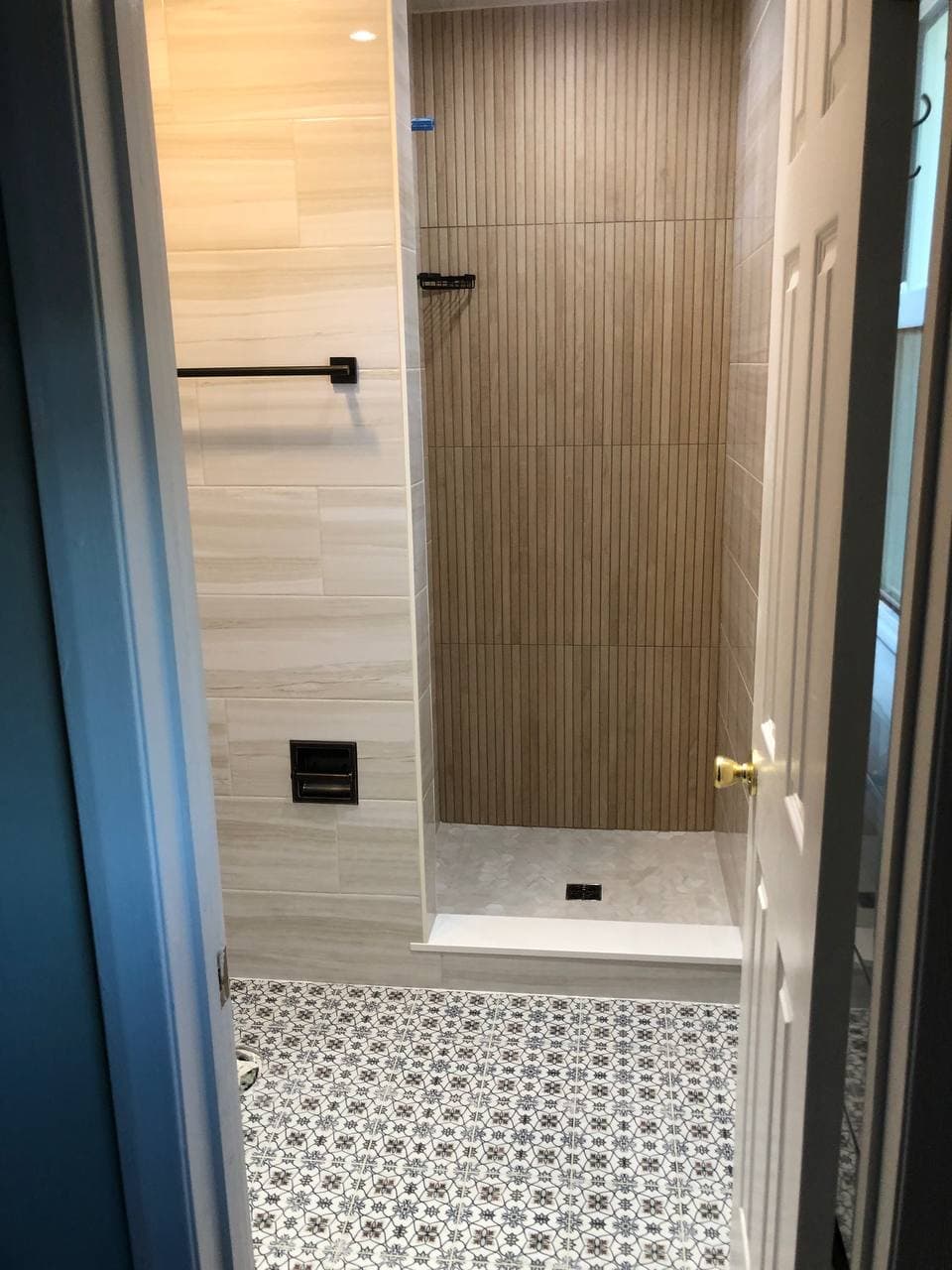 Finished walk-in shower with gray wall tile, mosaic floor, niche, and glass door