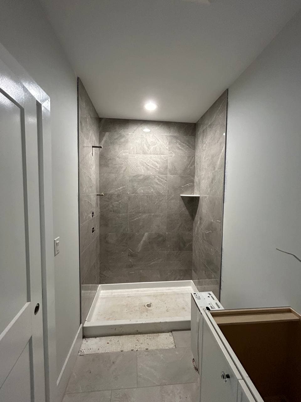 Bathtub surround finished with large gray tile and a recessed wall niche