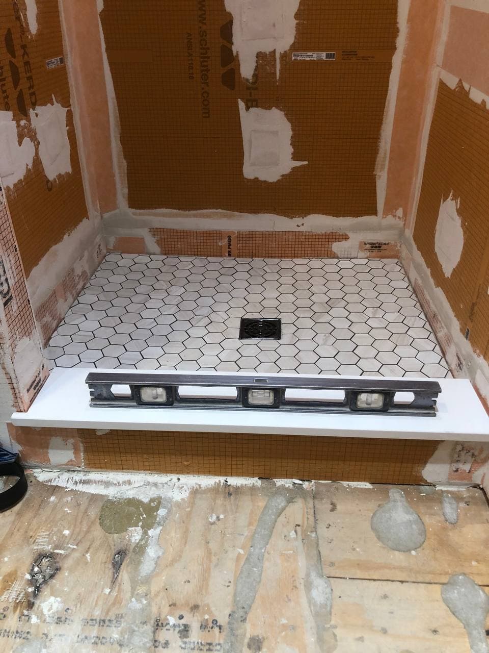 Mosaic shower floor being installed over a prepared shower base and curb