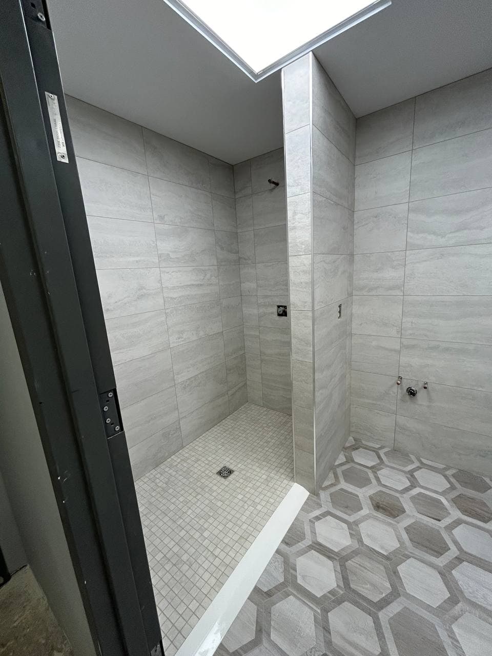 Entry view of a gray tiled walk-in shower with pebble floor and skylight