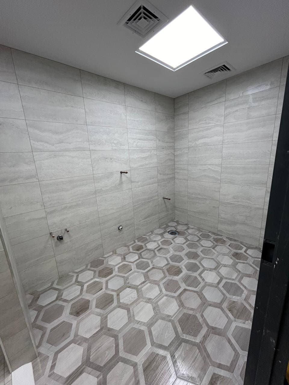 Walk-in shower with large gray wall tile, pebble floor, bench, niche, and skylight