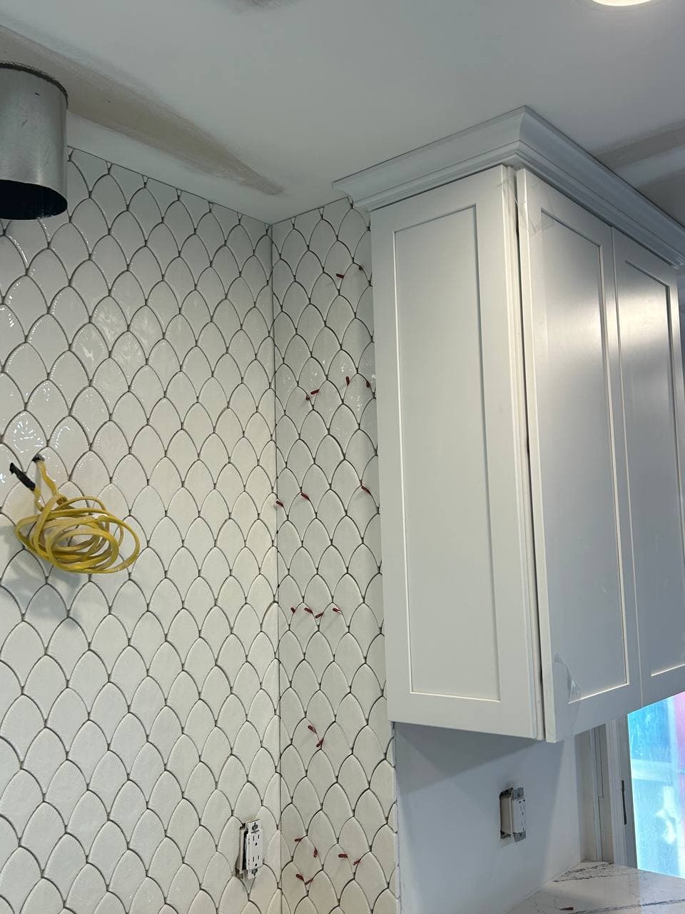 Diagonal white mosaic tile backsplash installed beside white kitchen cabinets
