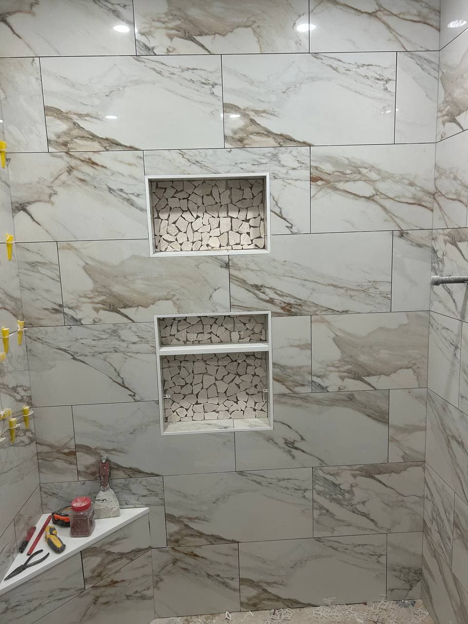 Marble-look shower wall tile with two recessed niches and mosaic niche backs