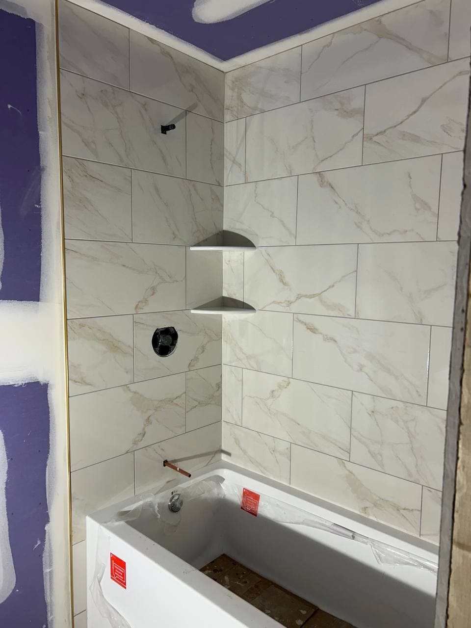 Marble-look wall tile installed around a bathtub with black shower fixtures