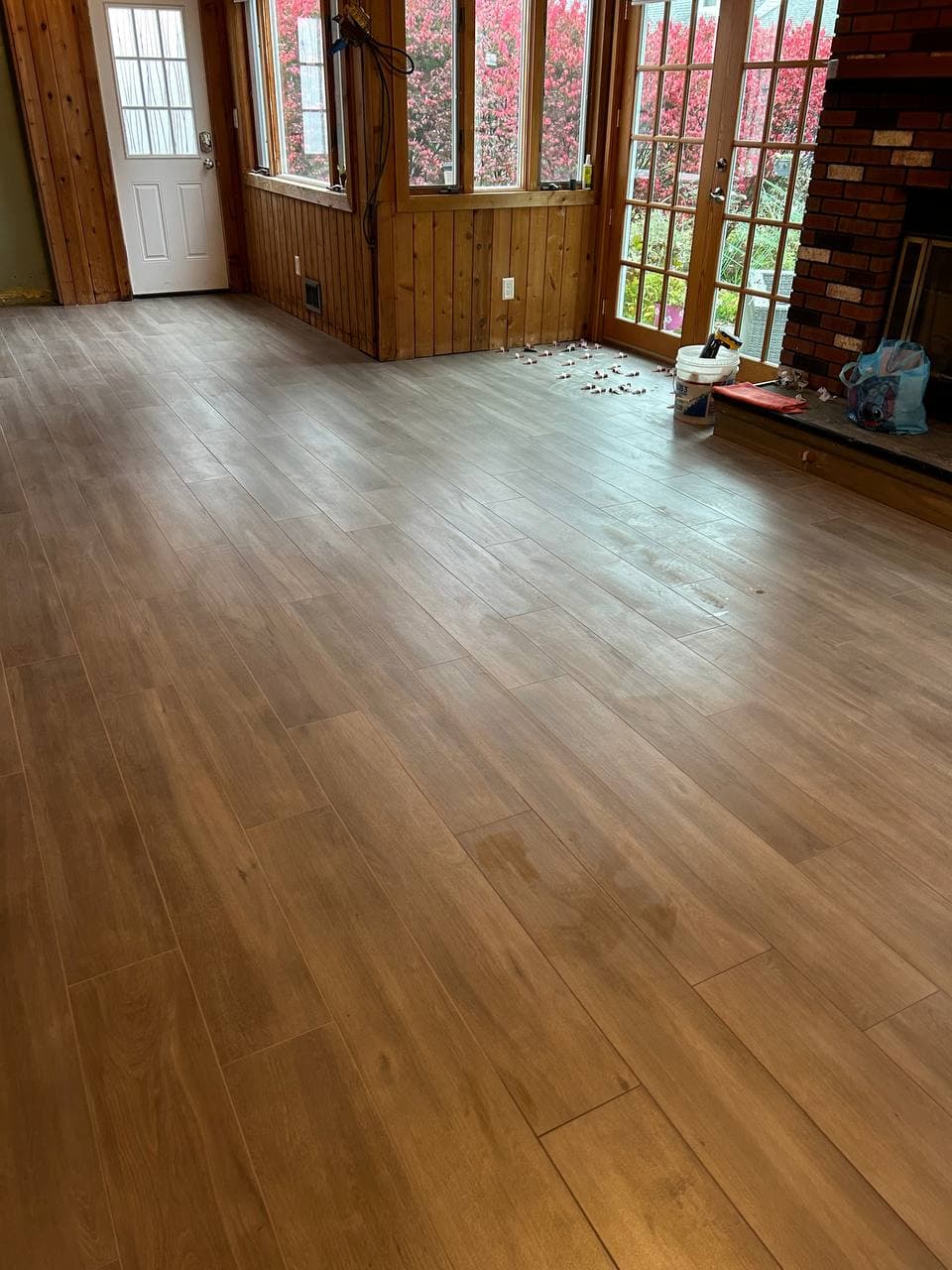 Warm wood-look tile floor installed in a bright entryway with glass doors